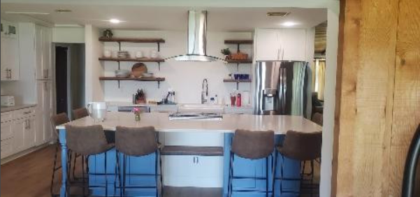 A kitchen with a large island , stools , a refrigerator and a stove.