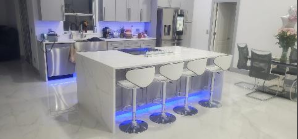 A kitchen with a large island , stools , and a refrigerator.