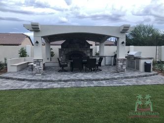 A patio with a fireplace and a table and chairs under a pergola.