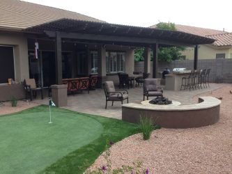 A patio with a fire pit and a putting green in front of a house.