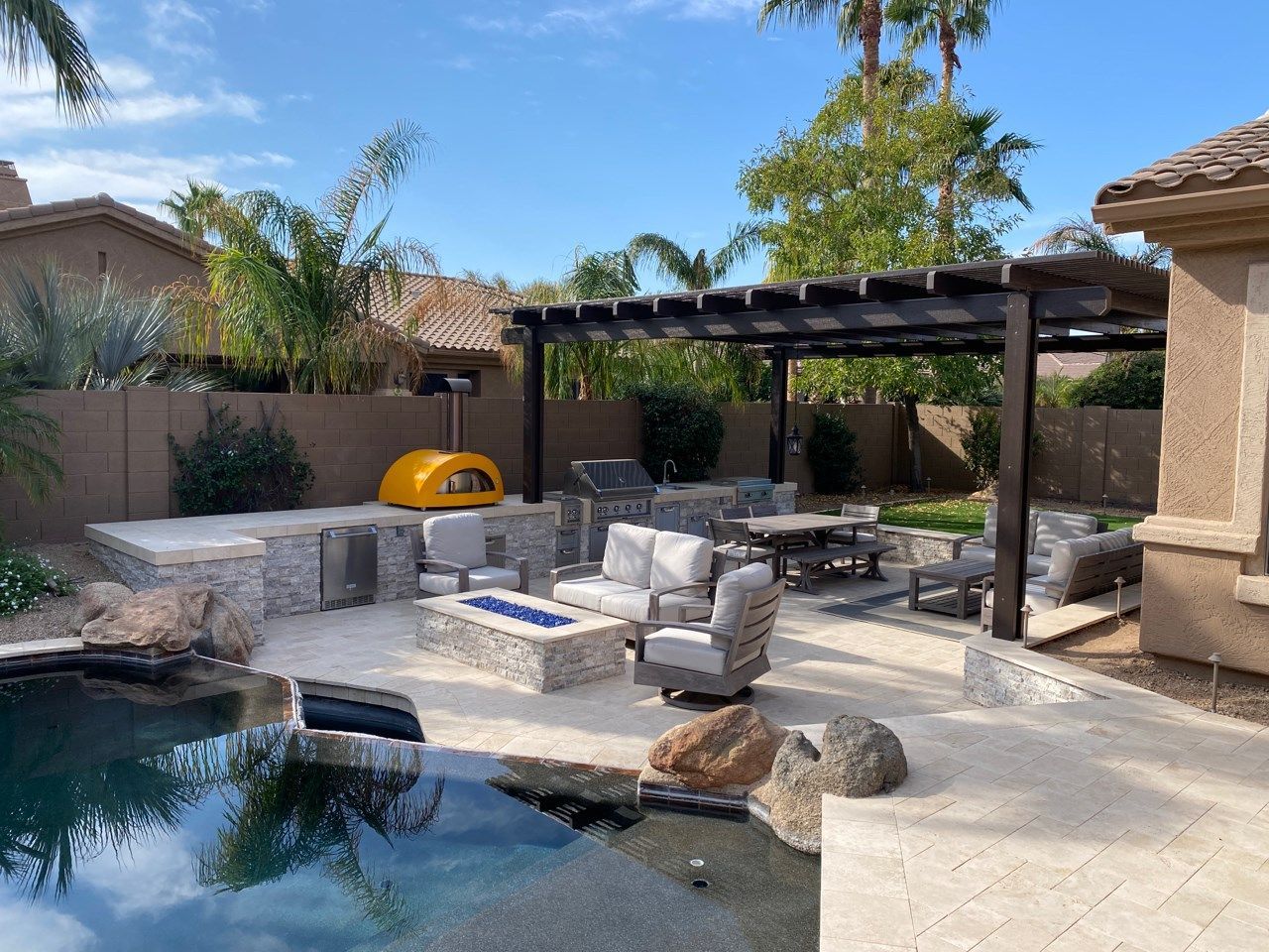 A patio with a fire pit and a pergola overlooking a pool.