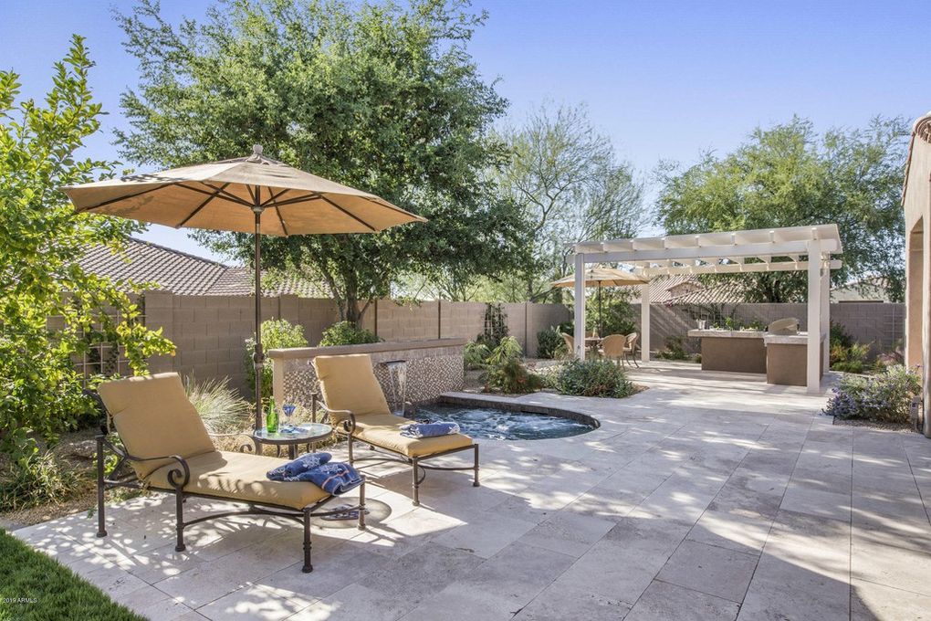 A patio with chairs , an umbrella and a hot tub.