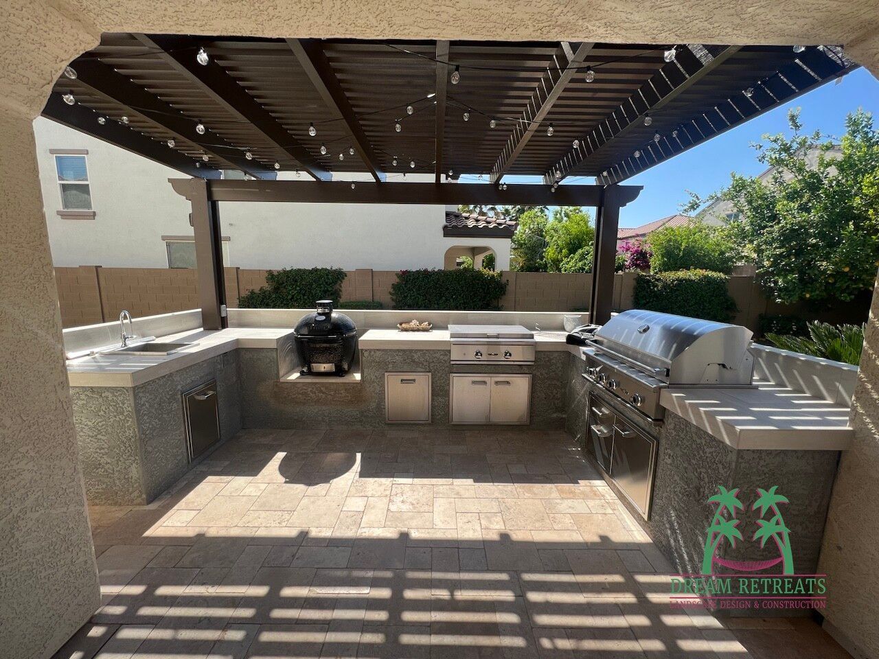 A large outdoor kitchen with a grill under a pergola.