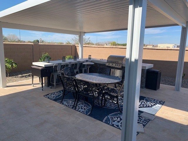 A patio with a table , chairs , and a grill under a canopy.