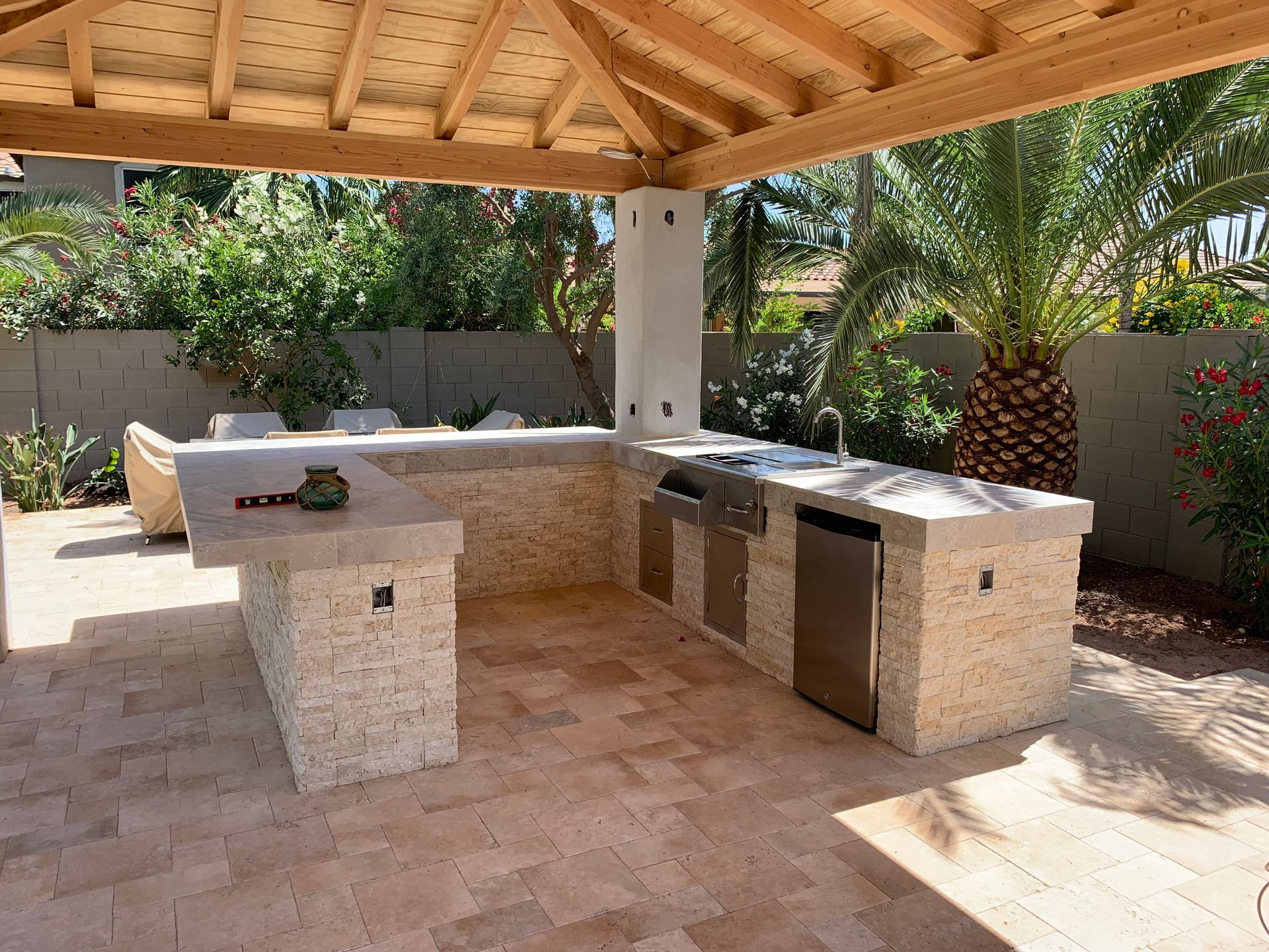 A large outdoor kitchen with a wooden roof and a brick floor