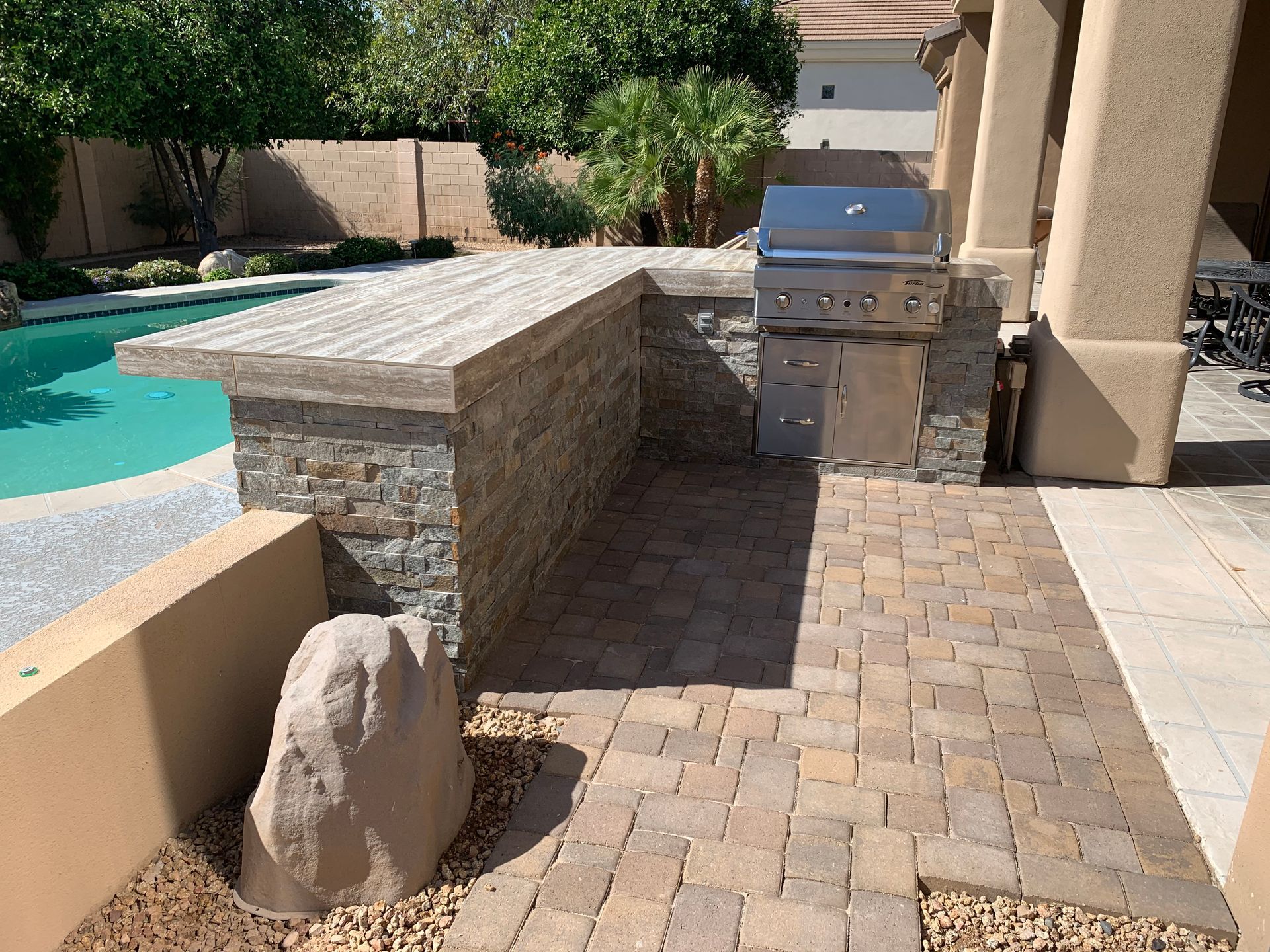 A patio with a grill and a pool in the background