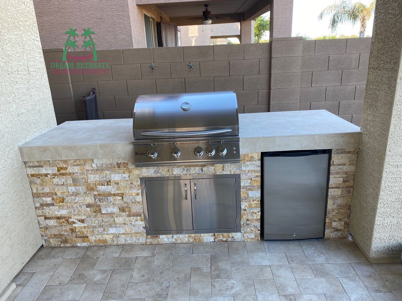 An outdoor kitchen with a grill and a refrigerator