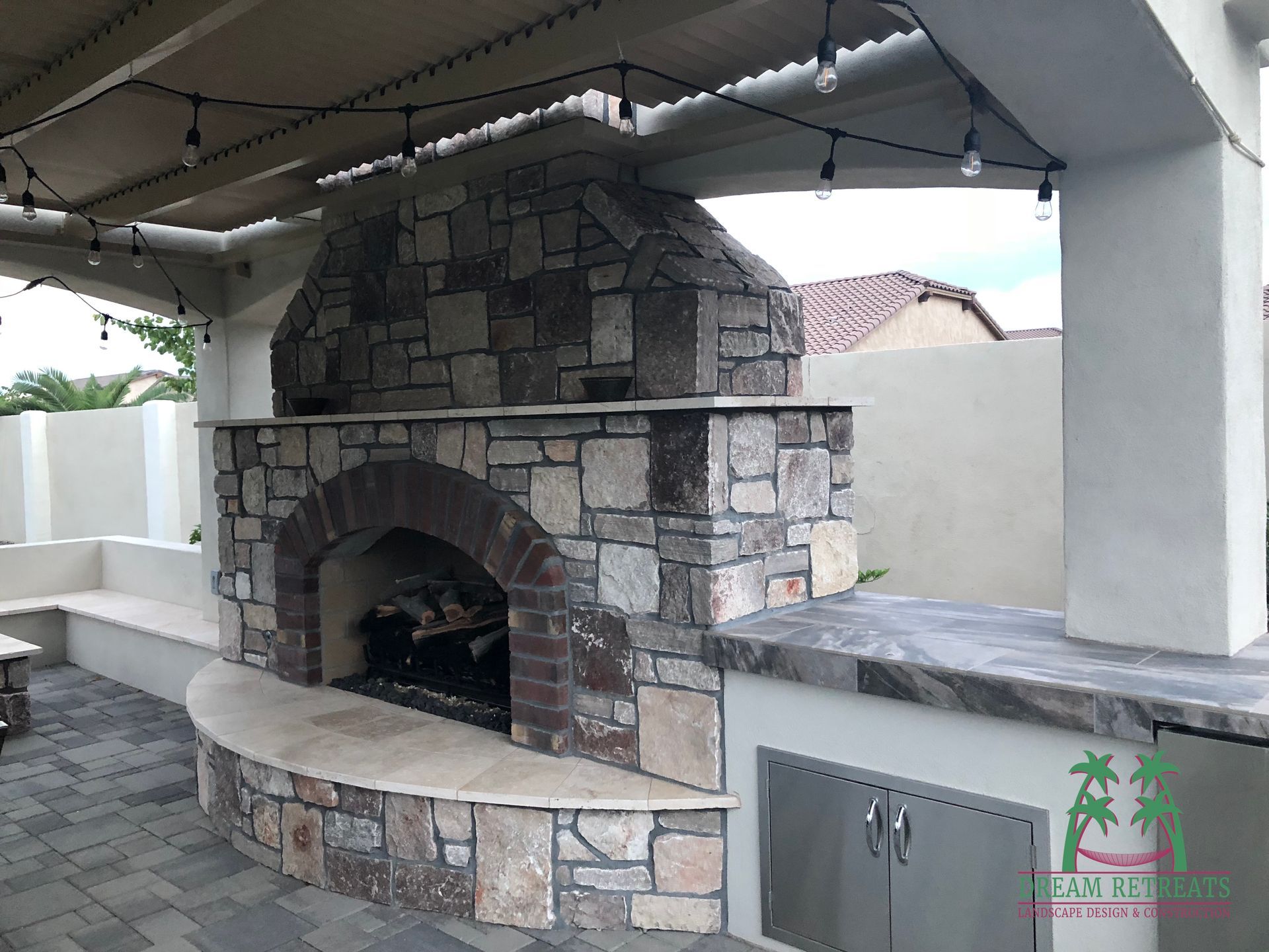 A stone fireplace is sitting under a covered patio area.