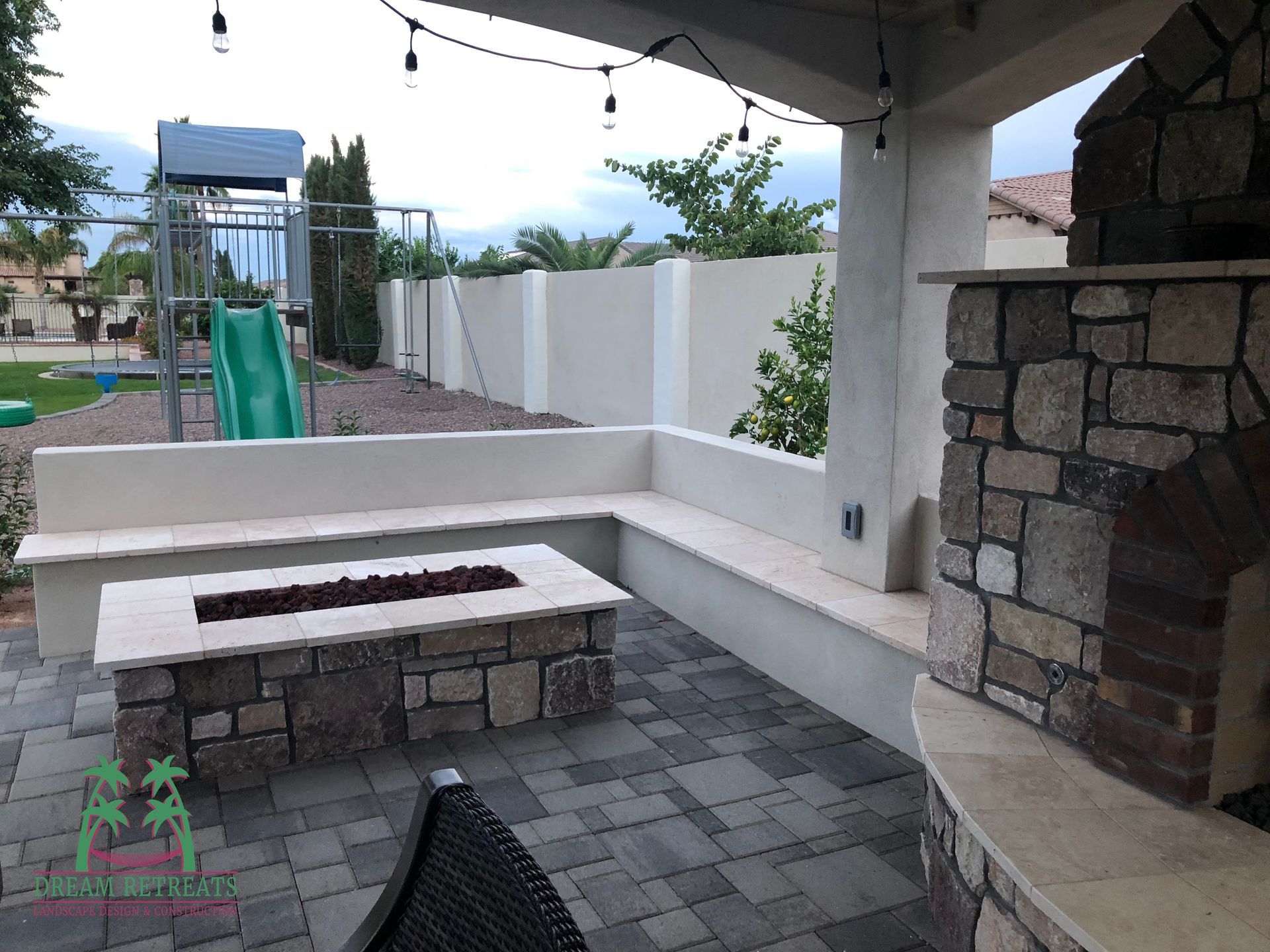 A patio with a fire pit and a playground in the background