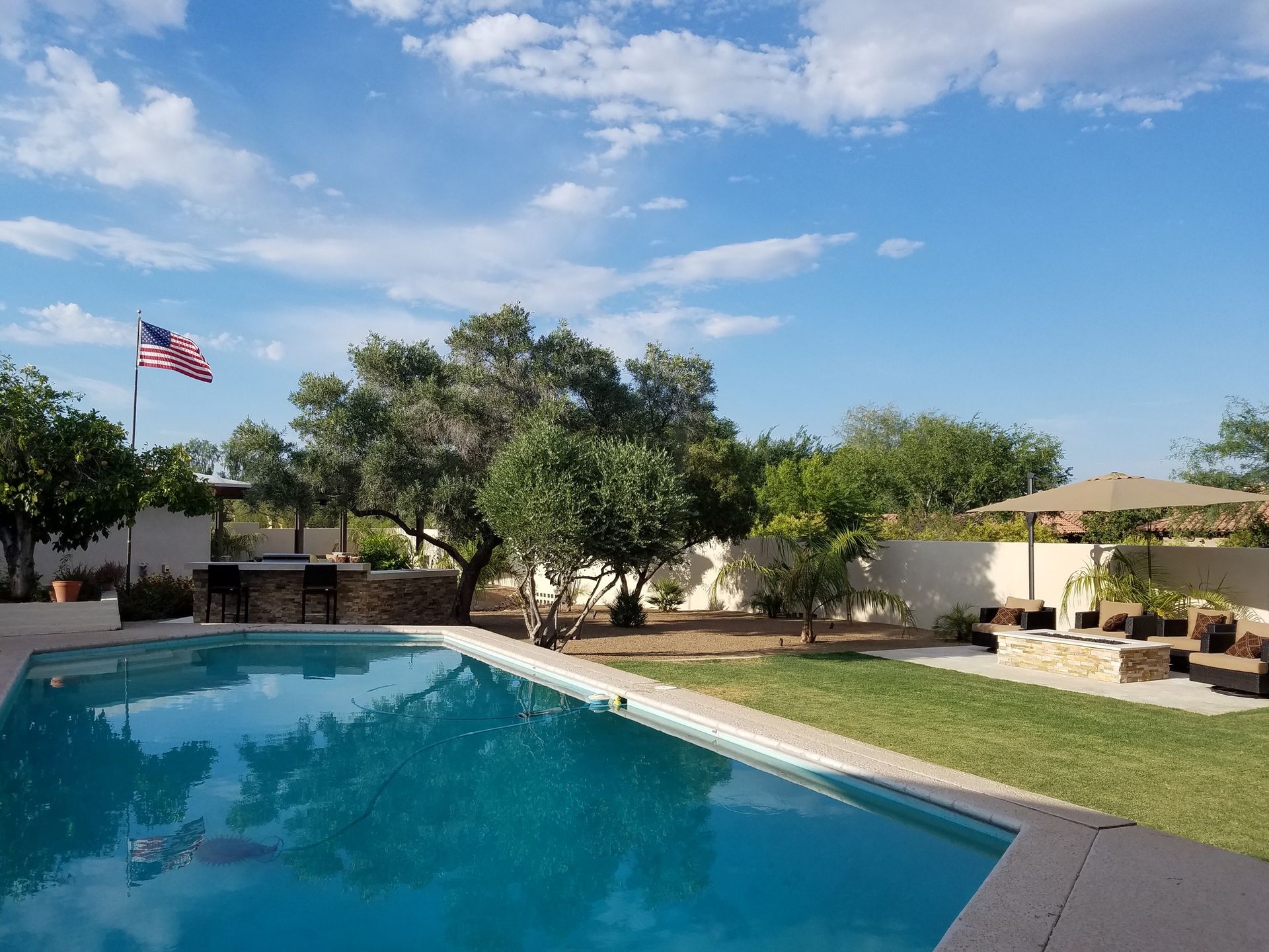 A large swimming pool is surrounded by trees and a flag.
