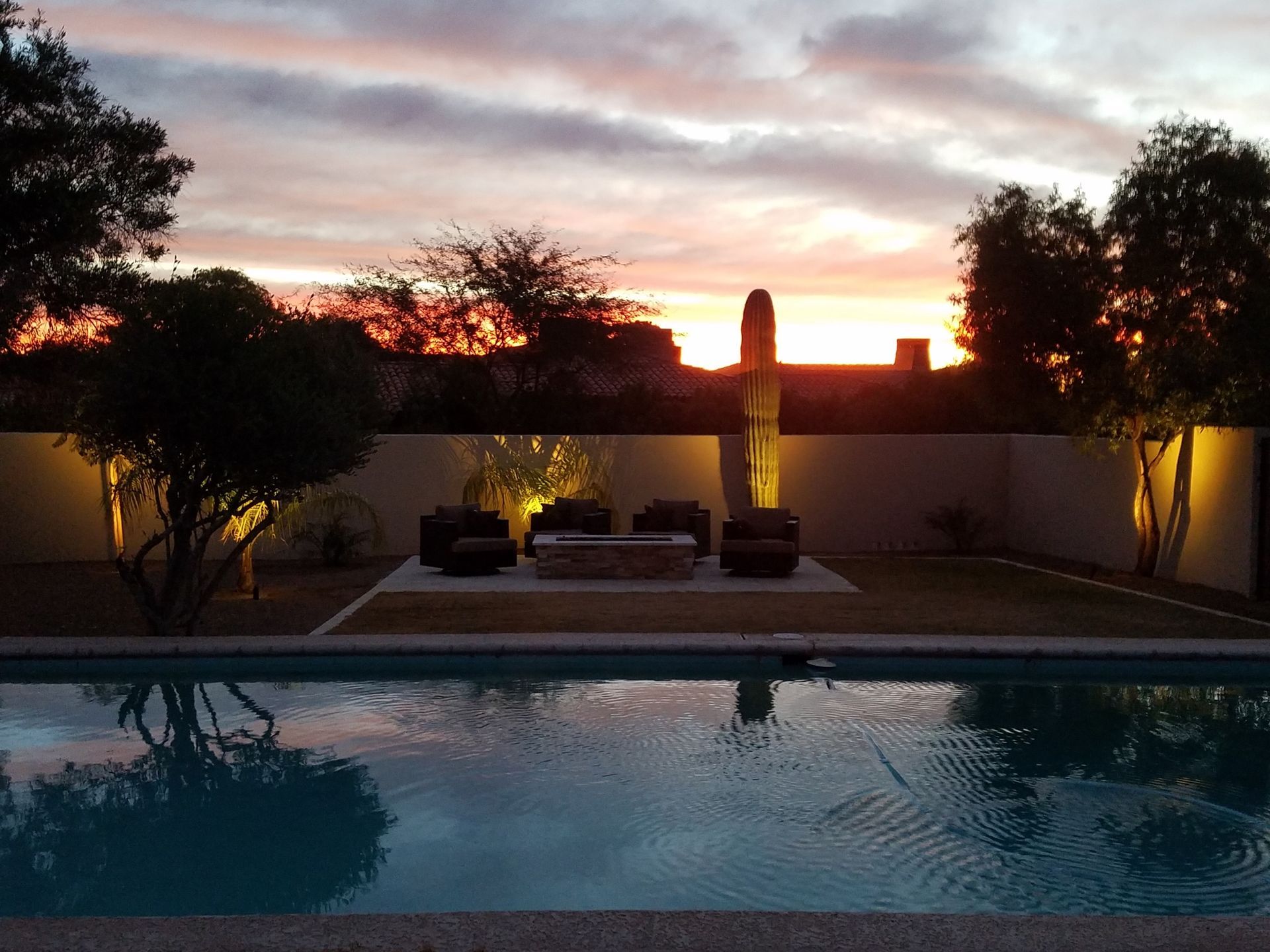 A sunset over a swimming pool with a fire pit in the middle