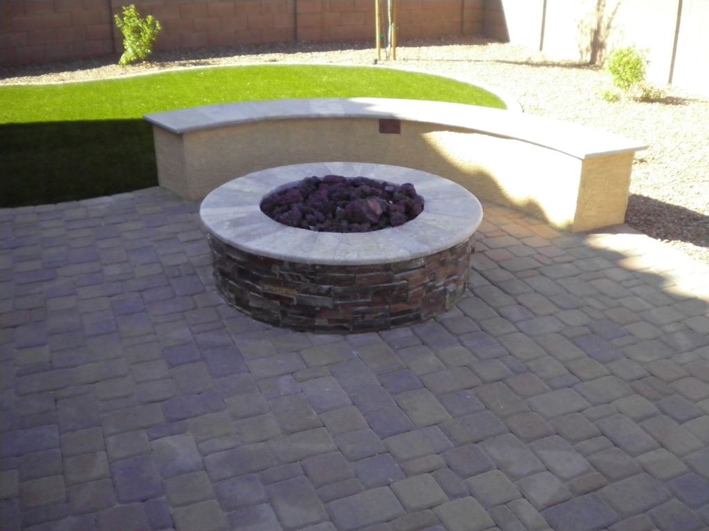 A fire pit sits on a brick patio next to a bench