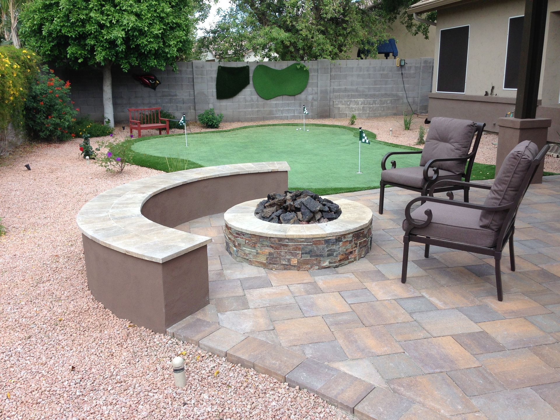 A patio with a fire pit and chairs in front of a putting green