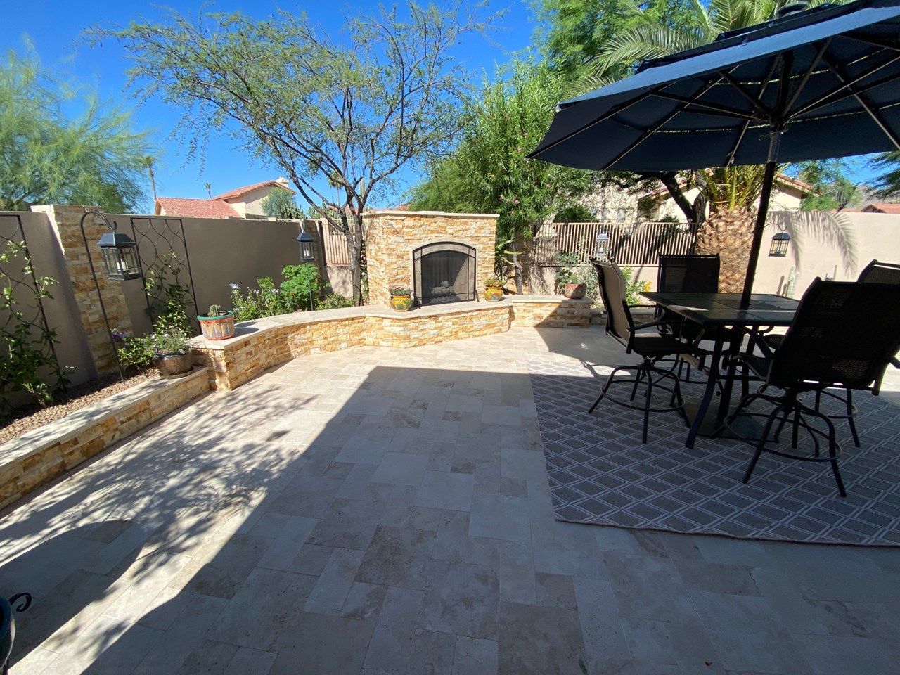 A patio with a table , chairs , umbrellas and a fireplace.