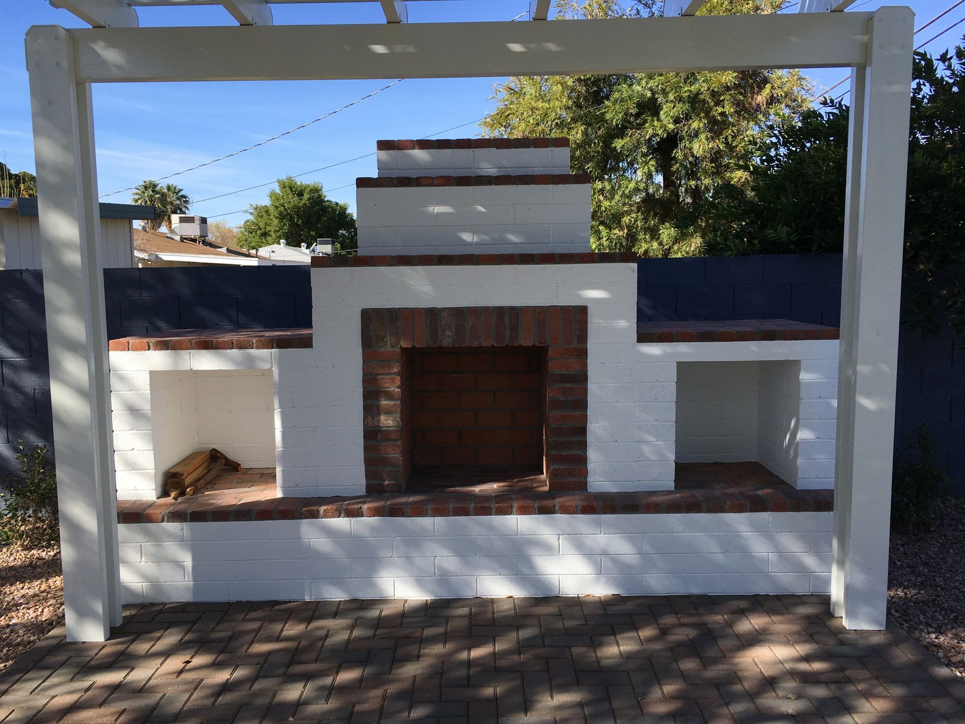 A brick fireplace under a white pergola on a patio