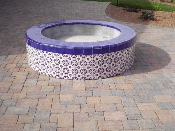 A circular planter with blue and white tiles sits on a brick patio