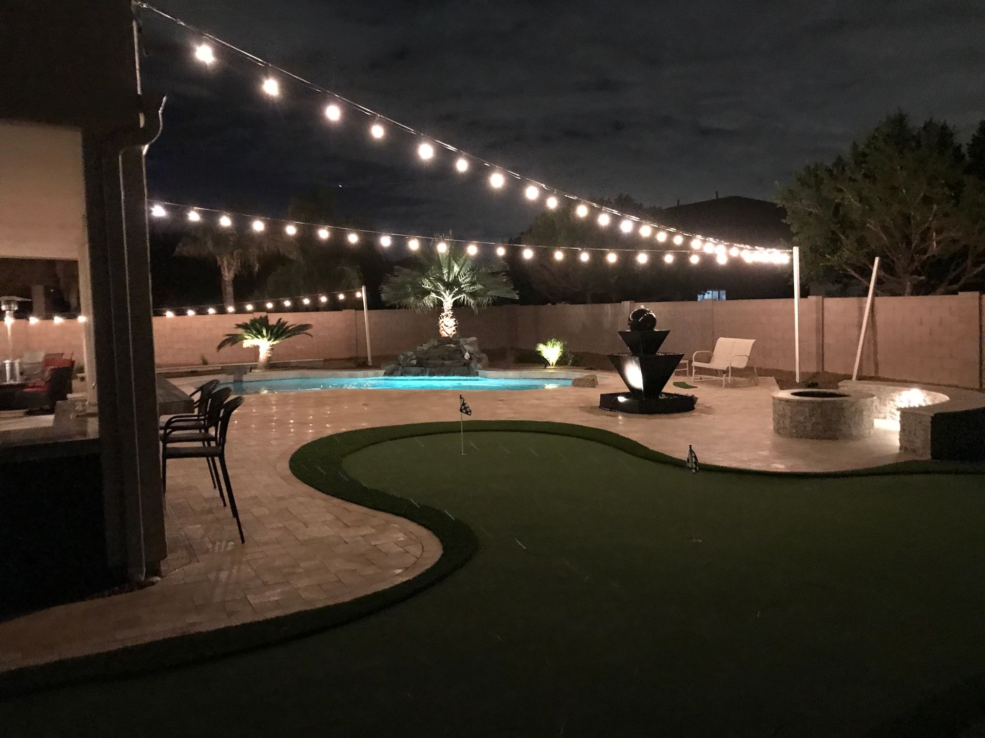 A backyard with a swimming pool and a putting green at night.
