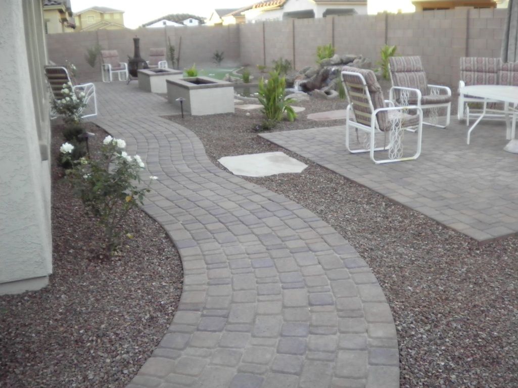 A brick walkway leading to a patio with chairs and a table