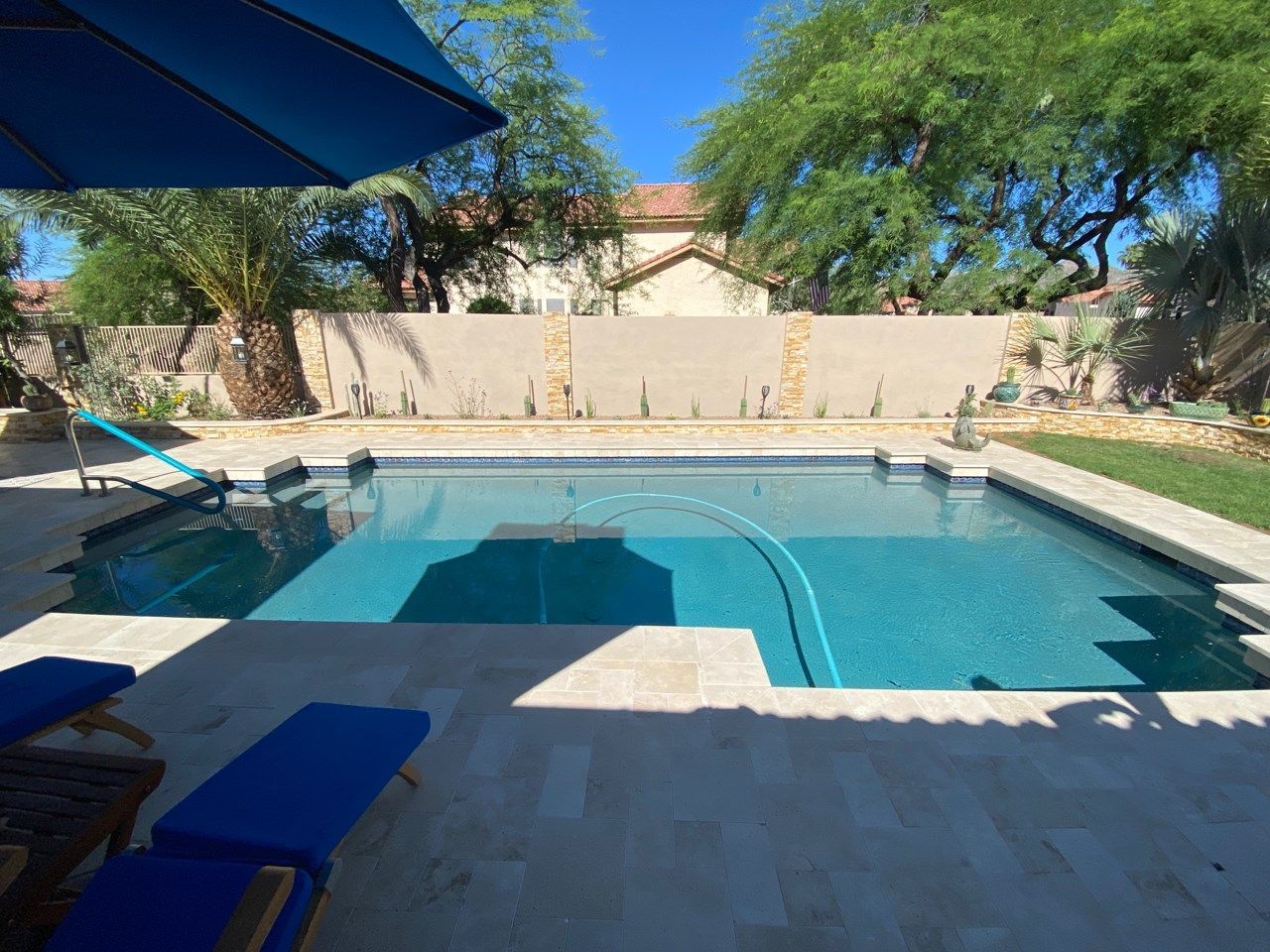 A large swimming pool with a blue umbrella and chairs