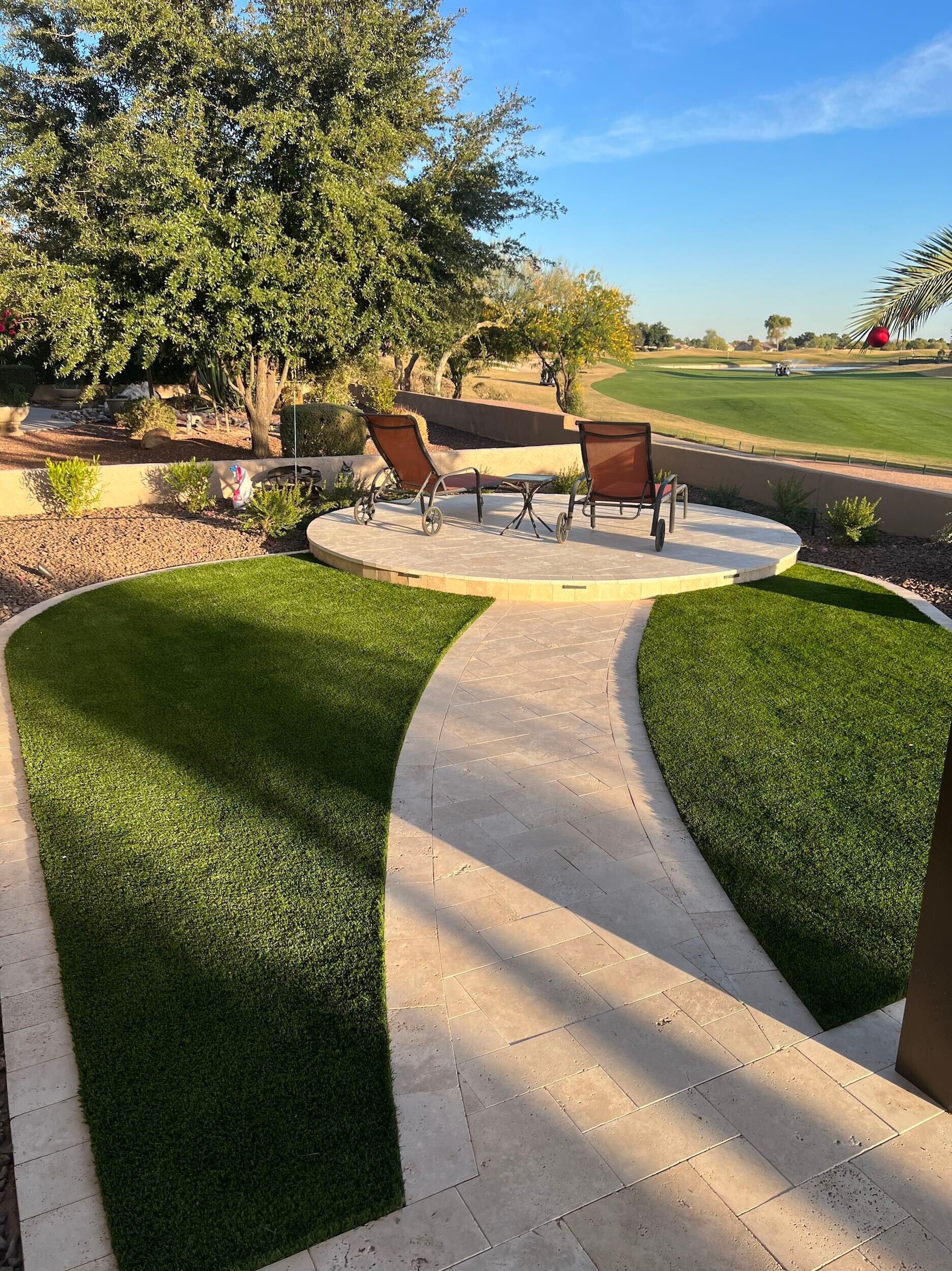 A patio with chairs and a table in the middle of a lush green field.