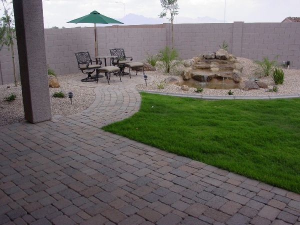 A patio with chairs and umbrellas and a waterfall in the backyard