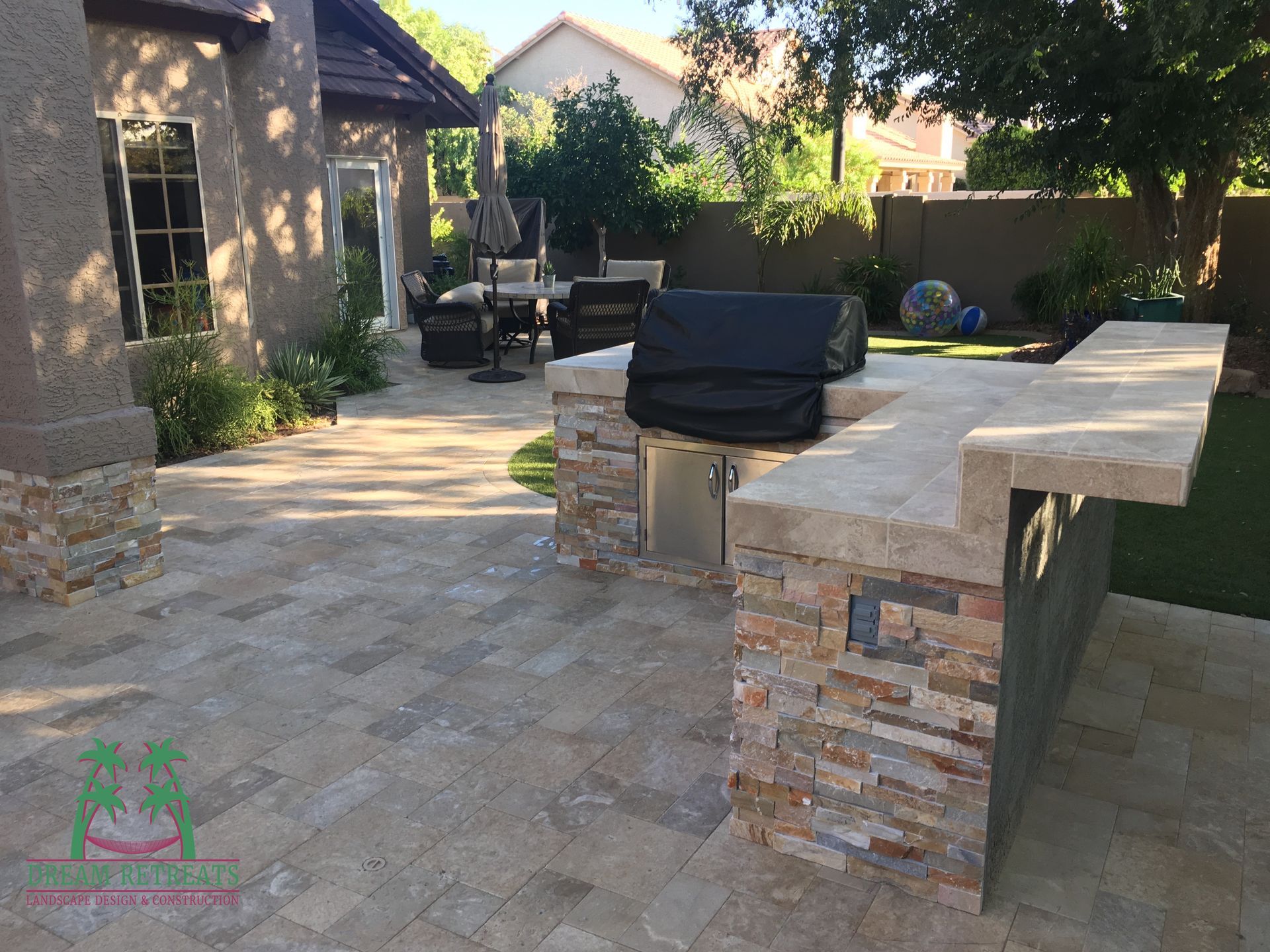 A grill is sitting on top of a stone counter in a backyard.