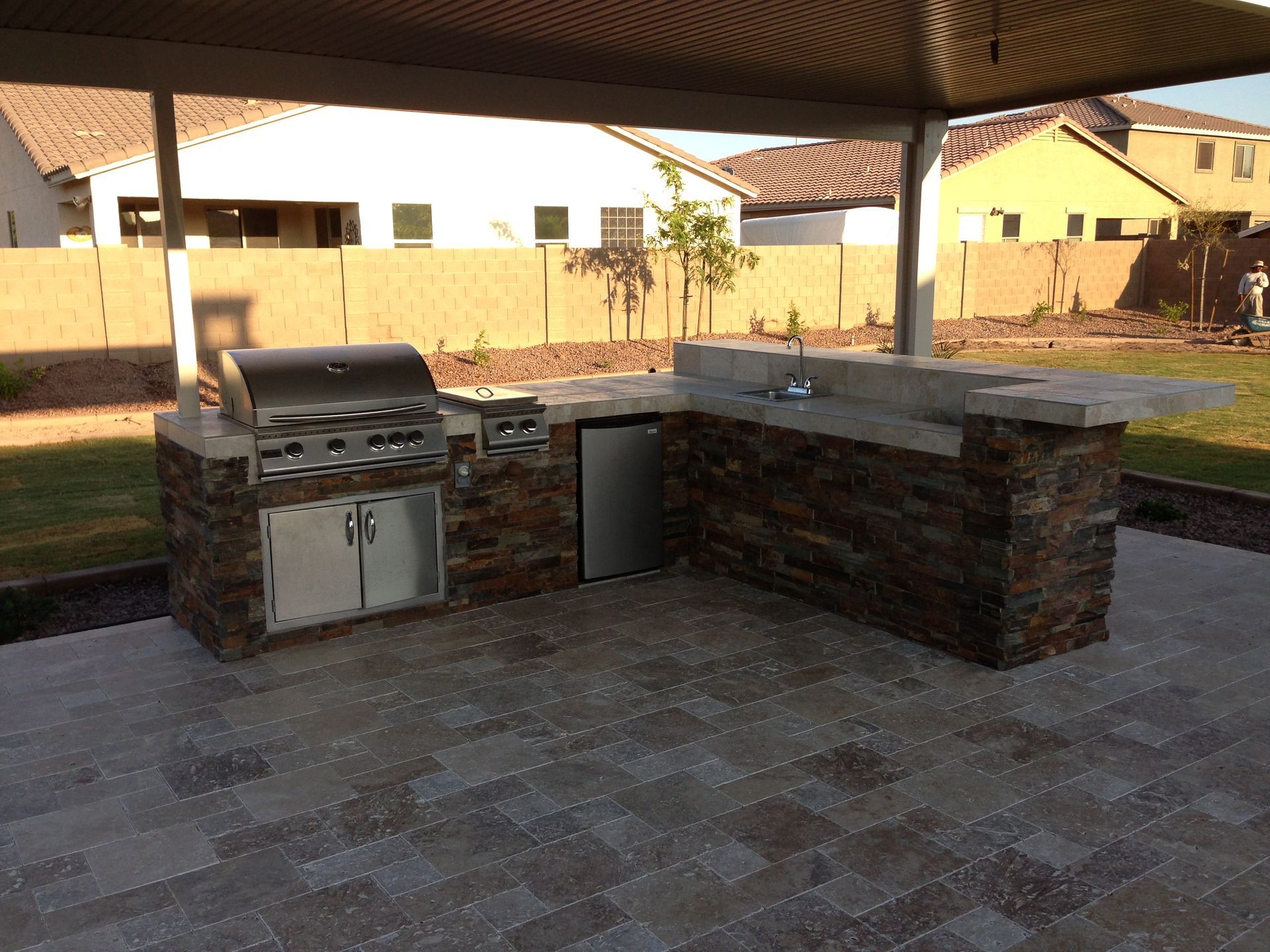 An outdoor kitchen with a grill and sink under a canopy