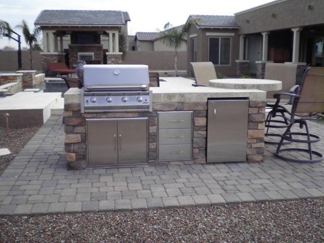 A brick patio with a grill and chairs in front of a house