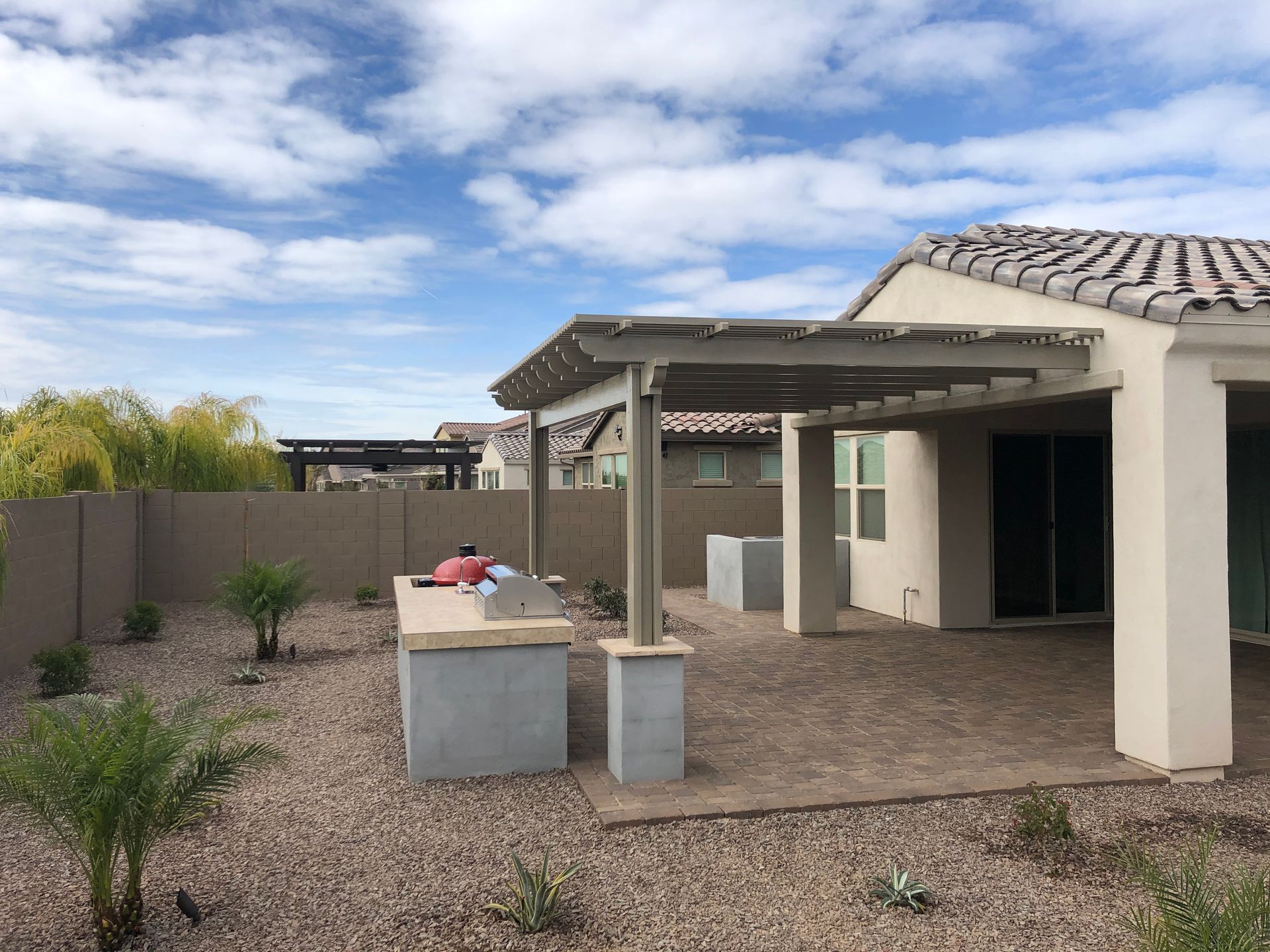 The backyard of a house with a pergola and a grill.