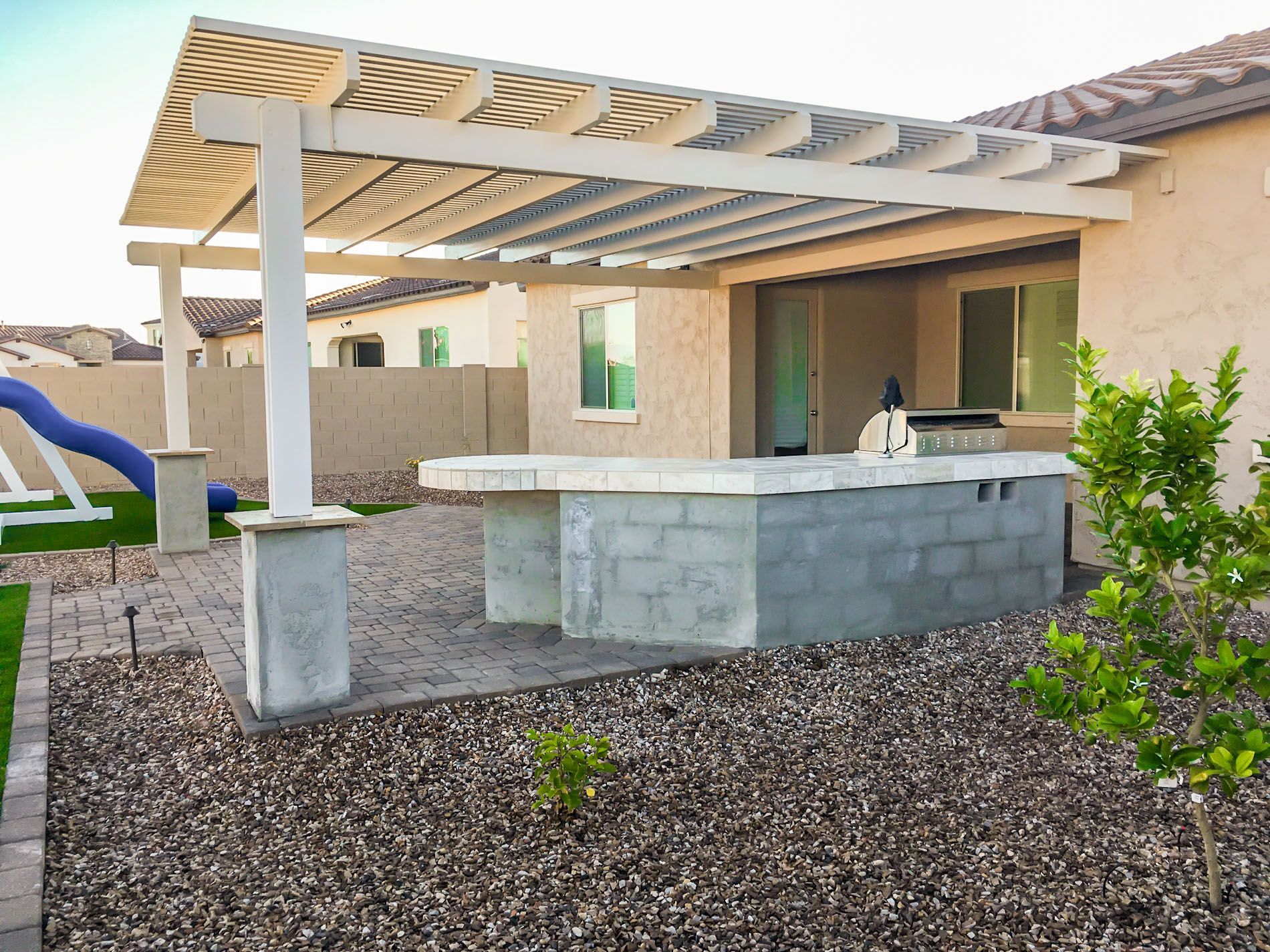 A patio with a pergola and a grill in the backyard of a house.