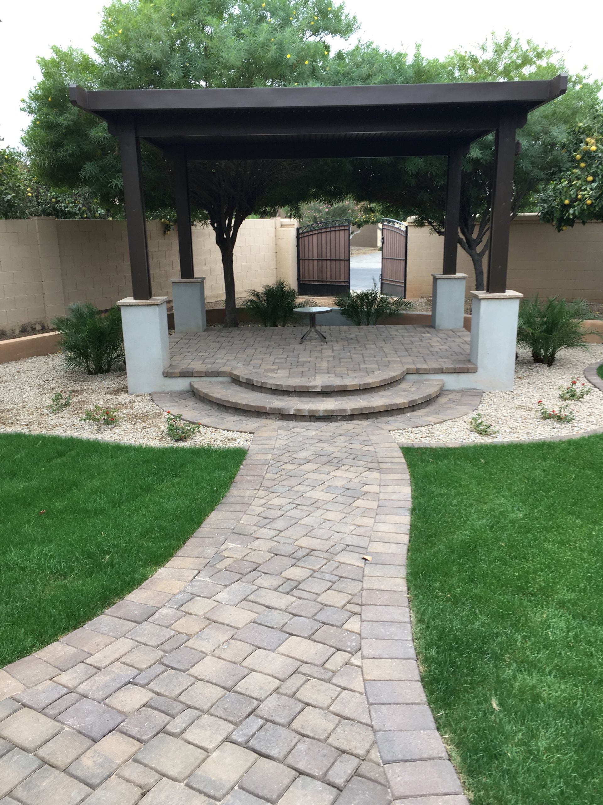 A brick walkway leading to a pergola in a backyard