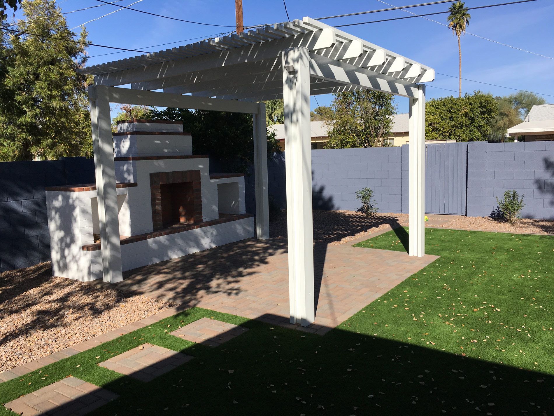A backyard with a white pergola and a fireplace.