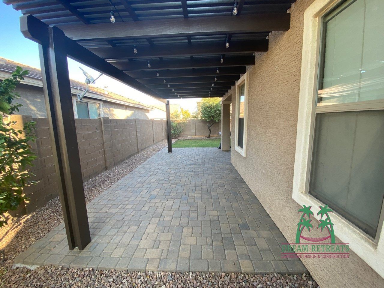 A patio with a pergola and brick pavers in front of a house.