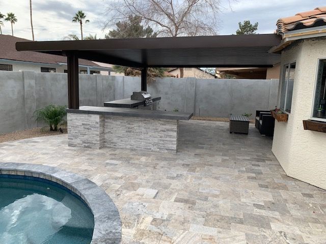 A patio with a grill and a pool in the background