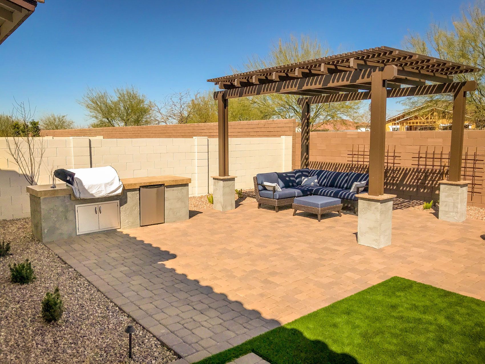 A patio with a grill , couch , chairs and a pergola.