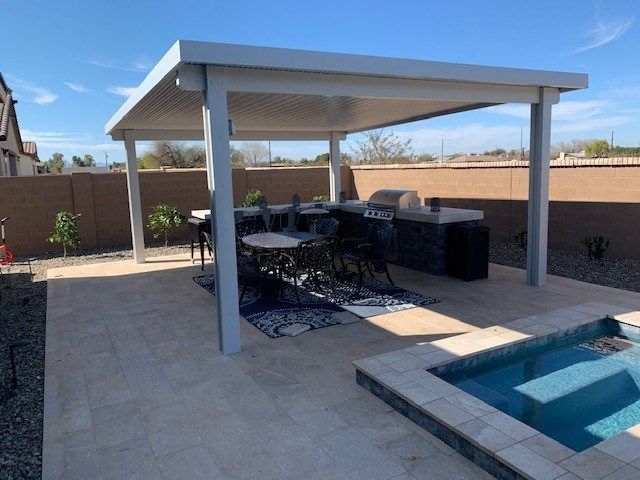 A patio with a table and chairs under a canopy next to a pool.