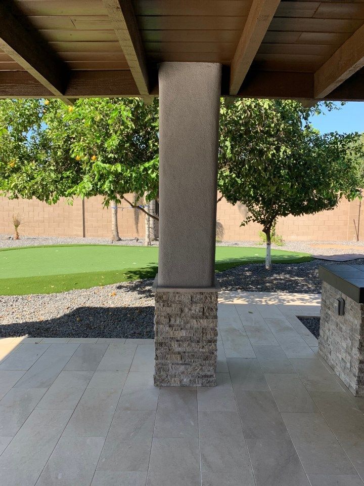 There is a pillar in the middle of a patio with trees in the background.