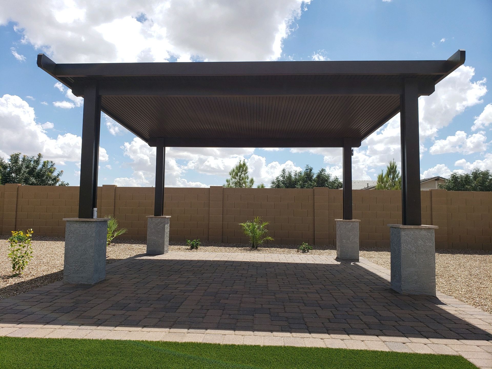 A pergola is sitting on top of a brick patio in a backyard.