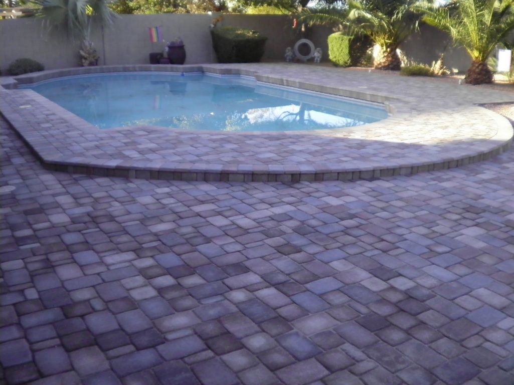 A large swimming pool is surrounded by a brick patio