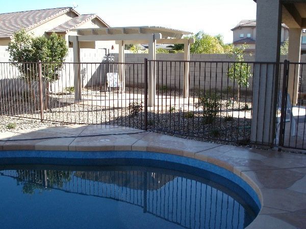 A fence surrounds a swimming pool with a pergola in the background