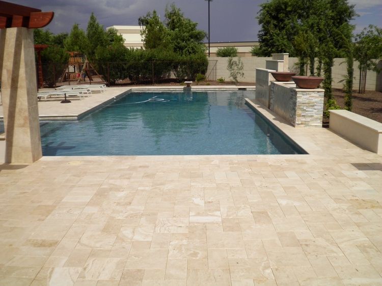 A large swimming pool is surrounded by a tiled patio