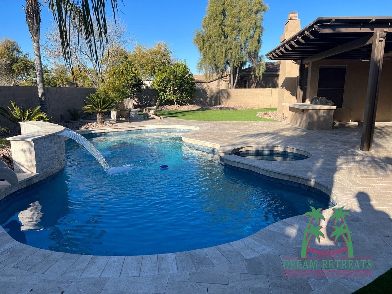 A large swimming pool with a waterfall in the backyard of a house.