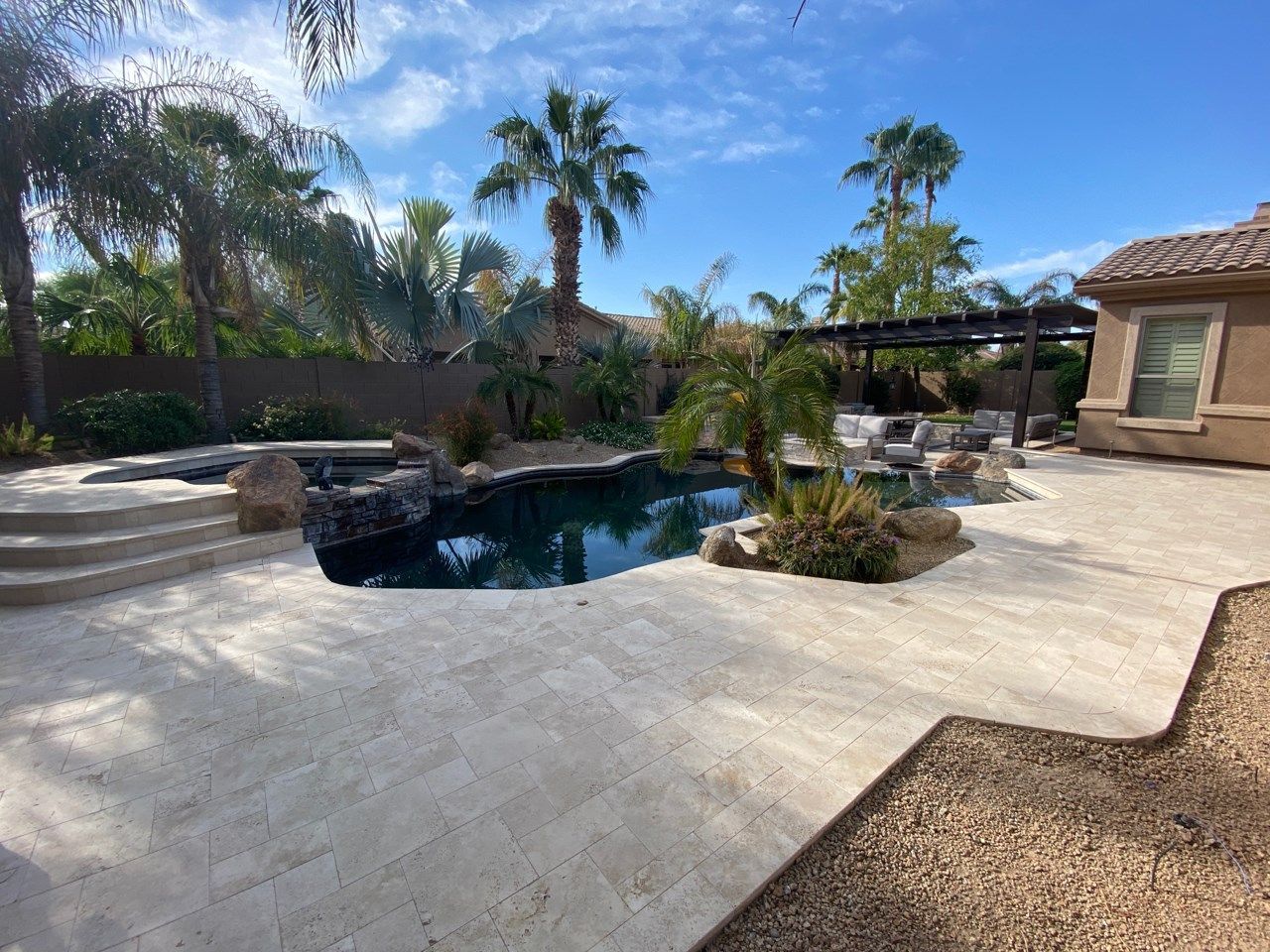 A large swimming pool is in the backyard of a house surrounded by palm trees.