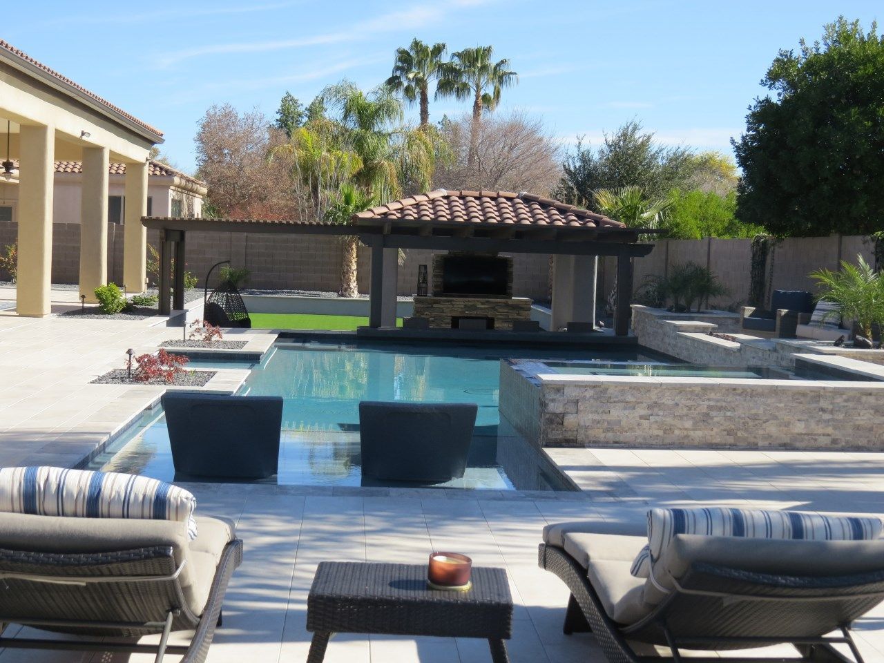 A patio with chairs and a table in front of a large swimming pool