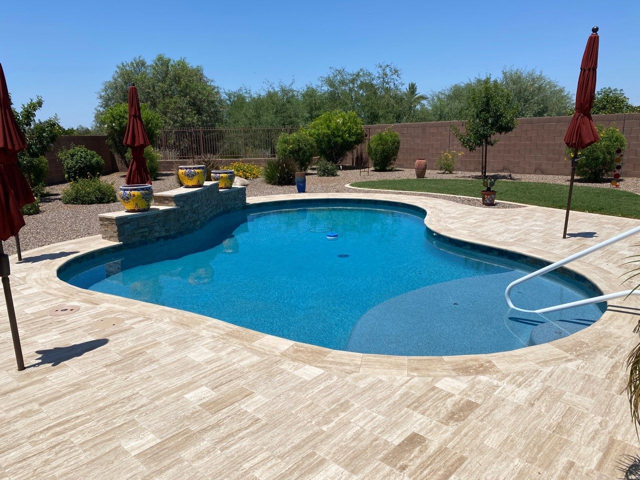 A large swimming pool is surrounded by umbrellas and potted plants.