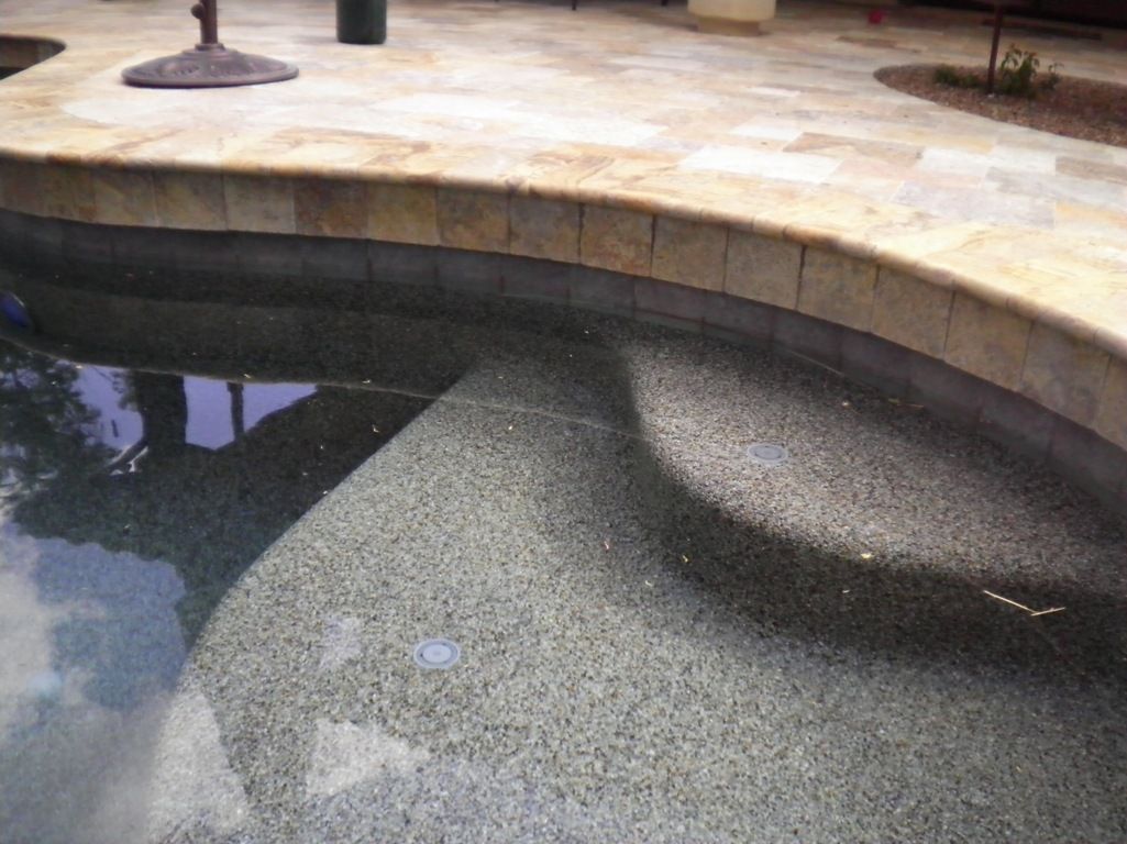 A swimming pool with steps and a patio in the background.