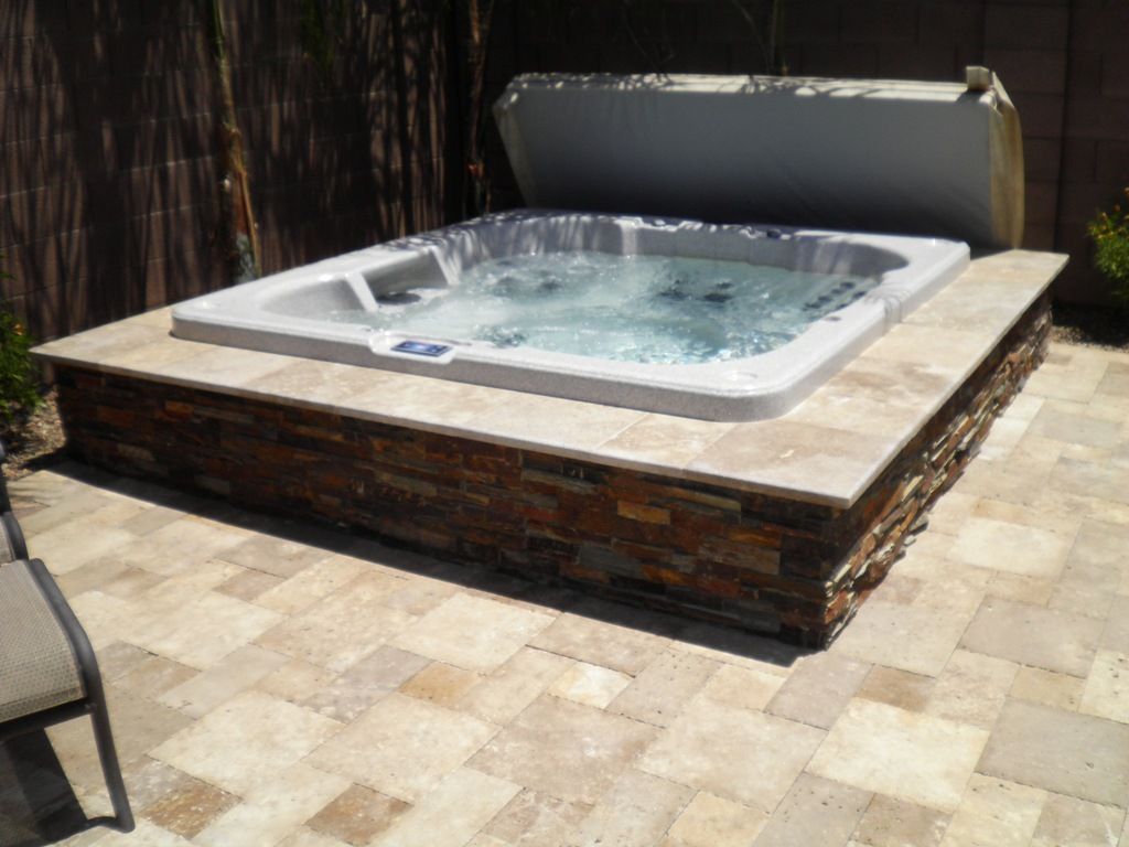 A hot tub is sitting on a tiled patio with the lid open.