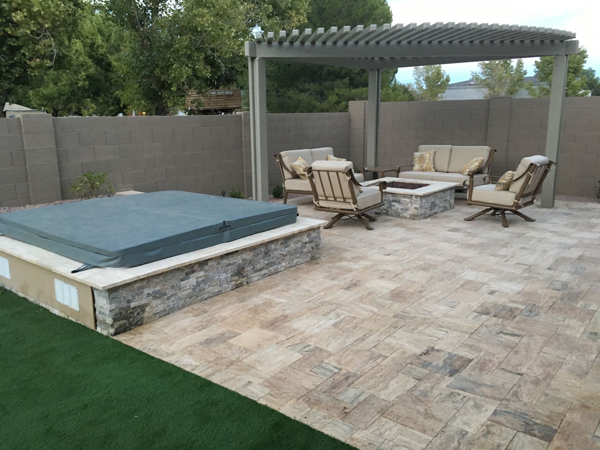 A patio with a hot tub , couch , chairs and a pergola.