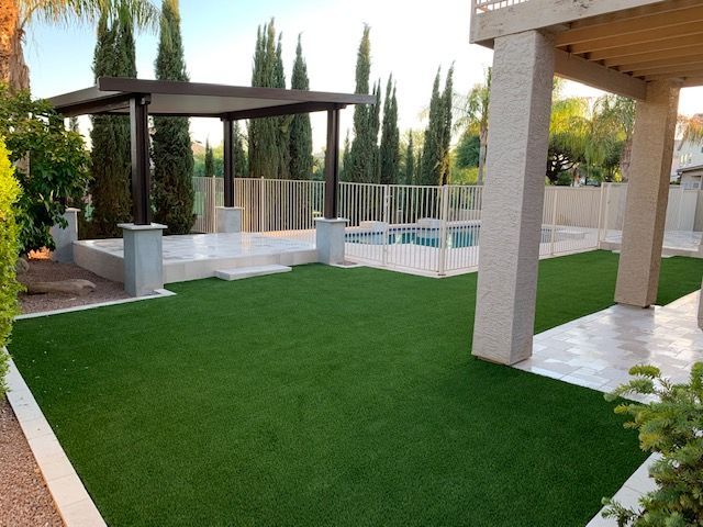 A lawn with a pergola and a pool in the background