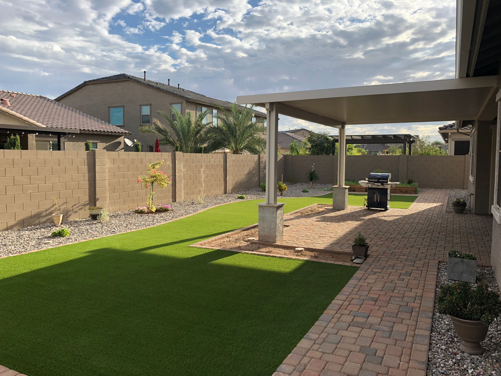 A backyard with a brick walkway and a covered patio.